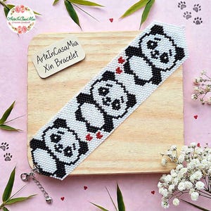 Può includere: Un braccialetto di perline intrecciate con un motivo ripetuto di tre panda neri e bianchi su sfondo bianco con piccoli cuori rossi. Il braccialetto include una chiusura a moschettone in metallo argentato e una catenella di estensione.