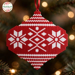 Può includere: Una decorazione natalizia a forma di diamante realizzata con piccole perline rosse e bianche. Il design presenta un motivo geometrico centrale affiancato da due fiocchi di neve bianchi su sfondo rosso, appeso a un sottile nastro rosso.