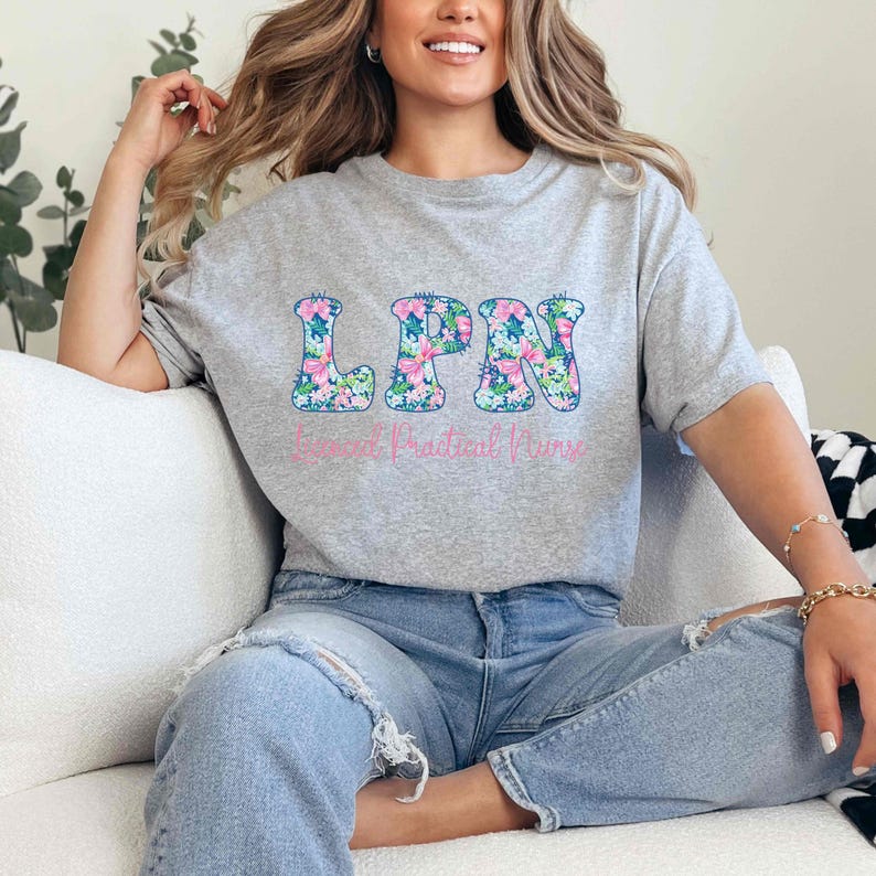 Puede incluir: Camiseta gris jaspeado con las letras "LPN" en un estampado floral. Debajo, las palabras "Licensed Practical Nurse" est&aacute;n impresas en rosa. La camiseta es de cuello redondo.