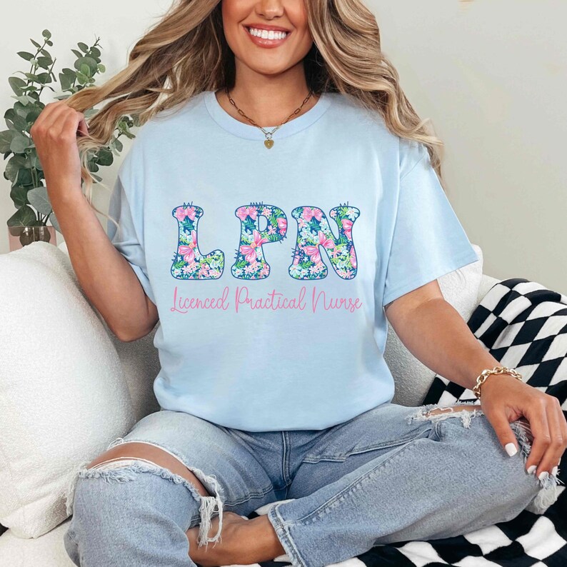 Puede incluir: Camiseta azul claro con las letras "LPN" en un estampado floral. Debajo de las letras est&aacute; el texto "Licensed Practical Nurse" en rosa. La camiseta se usa con vaqueros azules.