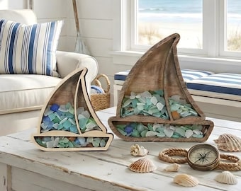 May include: Two wooden sailboat-shaped display frames filled with assorted sea glass in shades of blue, green, and white. The set includes several seashells and a round brass-colored compass resting on a white wooden surface.