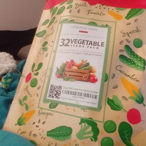 K&ouml;nnte beinhalten: Eine Packung mit 32 Gem&uuml;sesamen mit gelbem Hintergrund und bunten Illustrationen verschiedener Gem&uuml;sesorten. Die Packung enth&auml;lt einen QR-Code, den man f&uuml;r eine Anbauanleitung scannen kann. Der Text auf der Packung lautet "32 Vegetable Seeds Pack, Easy to grow, Non-GMO, High Germination."