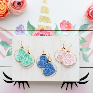 May include: Three pairs of crocheted heart earrings on a white background. The earrings are in pink, blue, and green.