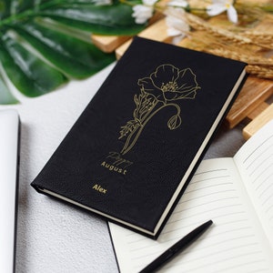 May include: Black leather journal with a gold poppy flower design and the text "Poppy August Alex".