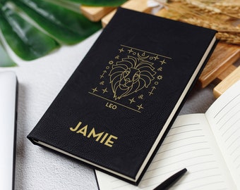 May include: Black leather journal with gold lettering. The journal has a gold lion zodiac symbol and the name "JAMIE" printed on the front.