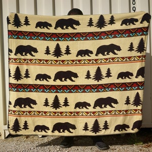 May include: A beige fleece blanket with a repeating pattern of black bears, pine trees, and a colorful geometric design.