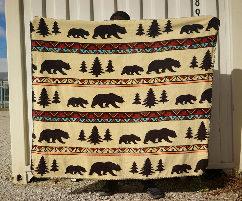 May include: A beige fleece blanket with a repeating pattern of black bears, pine trees, and a colorful geometric design.