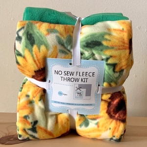 May include: A no-sew fleece throw kit with a sunflower print. The kit includes two pieces of fleece fabric and a cardboard template. The instructions on the packaging say "NO SEW FLEECE THROW KIT" and "12+ Ages".
