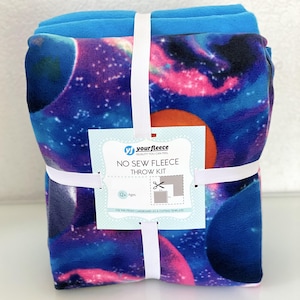 May include: A no-sew fleece throw kit with a galaxy print featuring blue, pink, and orange colors. The kit includes two pieces of fleece fabric and a cardboard template. The packaging includes the text "YourFleece Quality You Can Feel No Sew Fleece Throw Kit 12+ Ages Use this front cardboard as a cutting template!"
