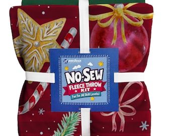 May include: A folded red fleece throw kit featuring a holiday pattern of gold stars, candy canes, red ornaments, and pine branches. A blue square label is centred on the front with white text reading NO-SEW FLEECE THROW KIT.