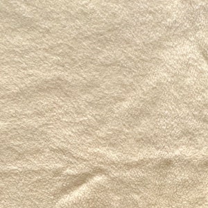 May include: A close-up of a soft, cream-colored fabric with a fuzzy texture. The fabric is slightly wrinkled and has a subtle sheen.