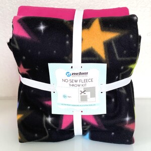 May include: A no-sew fleece throw kit with a black background and colorful stars. The kit includes two pieces of fleece fabric, one with a pink background and one with a black background. The kit is packaged with a white elastic band and a label that reads "your fleece" and "No Sew Fleece Throw Kit".