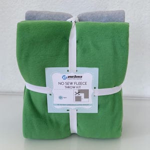 May include: A green fleece throw kit with a grey fleece roll on top, secured with white elastic. The kit includes a tag that reads "No Sew Fleece Throw Kit" and the brand name "yourfleece".