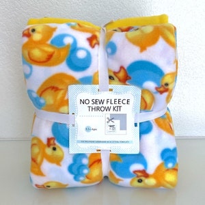 May include: A bundled fleece throw kit featuring a repeating pattern of orange rubber ducks and blue bubbles on a white background. The kit includes a yellow fleece edge and a tag that reads "NO SEW FLEECE THROW KIT".