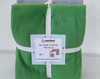 May include: A green fleece throw kit with a gray fleece roll on top, tied with white elastic. The kit includes a tag that reads "No Sew Fleece Throw Kit" and the brand name "yourfleece".