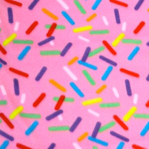 Puede incluir: Tela rosa con un patr&oacute;n de chispas de colores en rojo, naranja, amarillo, verde, azul, morado y blanco. Las chispas est&aacute;n dispersas sobre el fondo rosa.