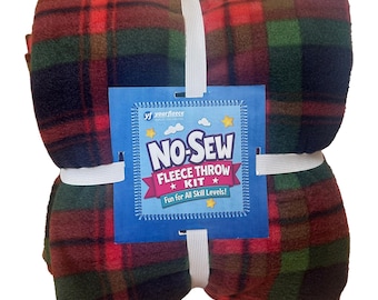 May include: A folded fleece throw kit featuring a red, green, and navy blue plaid pattern. The fabric is secured with white elastic bands and a blue square product label that reads "NO-SEW FLEECE THROW KIT" and "Fun for All Skill Levels!"