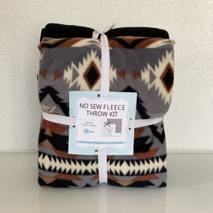 May include: A no-sew fleece throw kit with a geometric pattern in shades of brown, gray, black, and white. The kit includes a 50 x 60 inch (127cm x 152cm) fleece blanket and instructions for assembly. The kit is suitable for ages 12 and up.