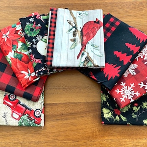 May include: A collection of Christmas-themed fabric squares with various patterns. Designs include red and black buffalo plaid, poinsettias, snowmen, a cardinal on a branch, Christmas trees, snowflakes, and holly. The fabrics are arranged on a wooden surface.