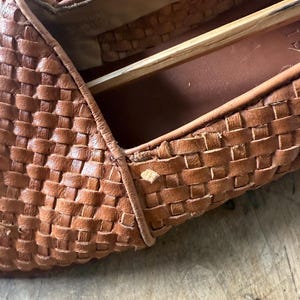 May include: Close-up of a pair of brown leather woven loafers. The shoes have a textured, basket-weave design. The interior of the shoe is visible, showing the insole and the wooden shoe form.