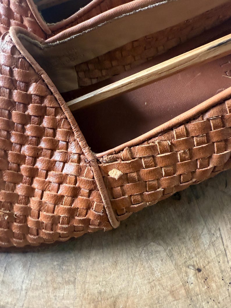 May include: Close-up of a pair of brown leather woven loafers. The shoes have a textured, basket-weave design. The interior of the shoe is visible, showing the insole and the wooden shoe form.