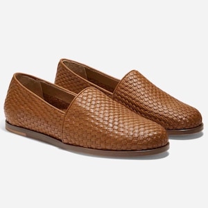 May include: A pair of brown woven leather loafers. The shoes have a slip-on design with a rounded toe and a flat sole. The woven pattern covers the entire upper of the shoe, giving it a textured appearance.