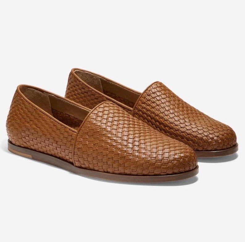 May include: A pair of brown woven leather loafers. The shoes have a slip-on design with a rounded toe and a flat sole. The woven pattern covers the entire upper of the shoe, giving it a textured appearance.