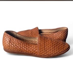 May include: A pair of brown woven leather loafers. The shoes have a slip-on design with a rounded toe and a low profile sole. The leather has a textured, basket-weave pattern.