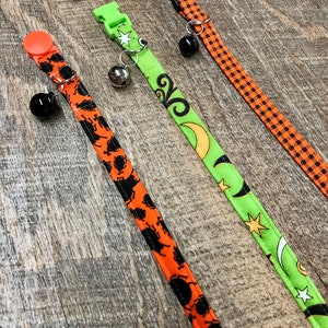 May include: Three Halloween-themed cat collars with bells. The collars are orange and black with different patterns, including stars, moons, and swirls.