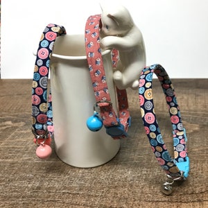 May include: Three colorful cat collars with button and spool patterns. The collars have bell charms and are adjustable.