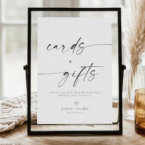 May include: A vertical rectangular sign in a thin black metal frame featuring white paper with black text that reads cards + gifts, thank you for celebrating our special day with us, and the names Susan and Andrew with the date 09.09.20XX.