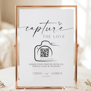 Op de afbeelding: Een wit rechthoekig bord in een roségouden metalen frame met de zwarte tekst capture THE LOVE, een camerapictogram met een QR-code, de woorden SCAN TO UPLOAD, SHARE YOUR PHOTOS WITH US, SIMPLE SCAN & UPLOAD!, CRISSY and ANDREW, en 12.12.20XX.