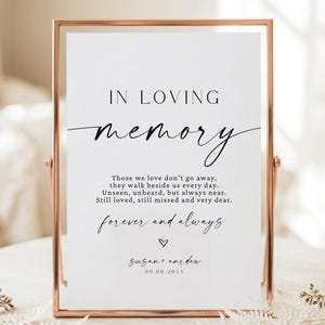May include: A vertical rectangular sign in a thin rose gold metal frame featuring black printed text that reads IN LOVING memory, followed by a poem, the phrase forever and always, a small heart icon, and the names Susan and Andrew with 00.00.20XX.