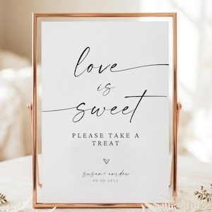 Puede incluir: Un letrero rectangular vertical en un marco de metal oro rosa con el texto negro "love is sweet PLEASE TAKE A TREAT", un pequeño icono de corazón, los nombres "Susan and Andrew" y la fecha "09.09.20XX" impresos sobre fondo blanco.
