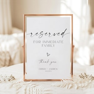 May include: A vertical rectangular sign in a rose gold metal frame. The white sign features black text that reads: reserved FOR IMMEDIATE FAMILY, a small heart icon, Thank you, CRISSY + ANDREW, and the date 12.12.20XX in a clean serif font.