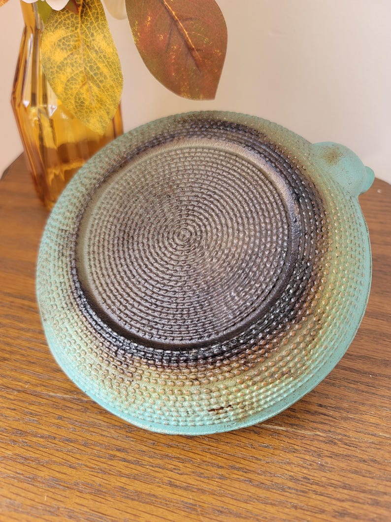 May include: A teal blue ceramic dish with a textured, woven pattern on the bottom. The dish has a slightly raised lip and a small handle on the side.