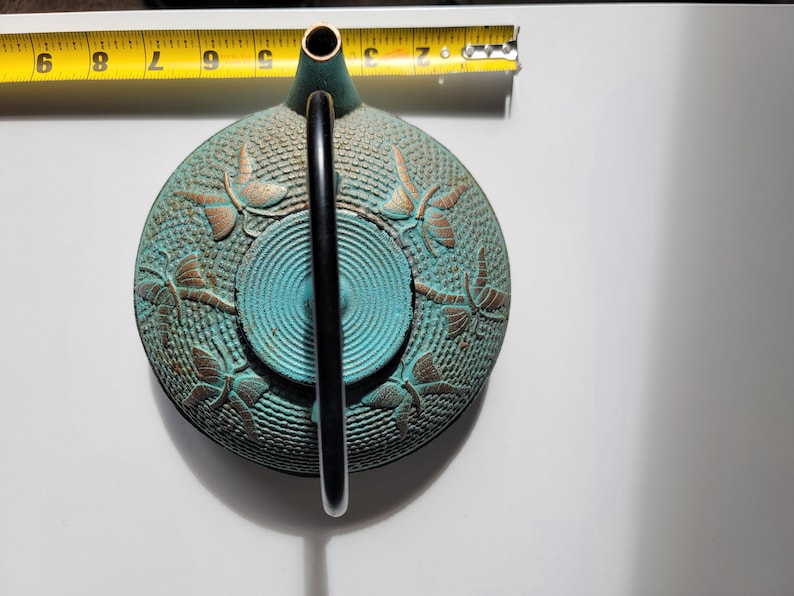 May include: A teal blue cast iron teapot with a black handle and gold dragonfly accents.