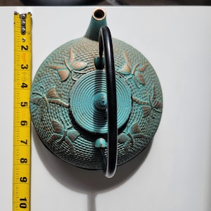 May include: A teal blue cast iron teapot with a black handle and gold dragonfly designs.