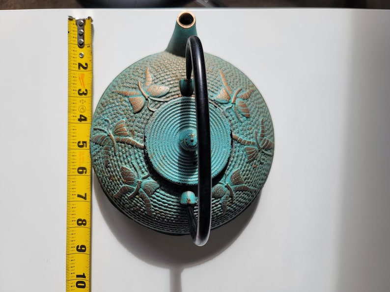 May include: A teal blue cast iron teapot with a black handle and gold dragonfly designs.