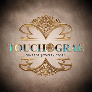 May include: Gold and blue logo for a vintage jewelry store called "Touchograe". The logo features a decorative, ornate design with a circular element in the center.