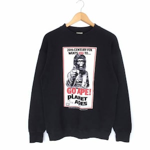 May include: Black crew neck sweatshirt with a graphic from the movie "Planet of the Apes." The graphic features a black and white image of an ape holding a gun, with the text "GO APE!" and "20th Century Fox wants you to..." in red and white.
