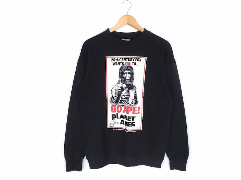 May include: Black crew neck sweatshirt with a graphic from the movie "Planet of the Apes." The graphic features a black and white image of an ape holding a gun, with the text "GO APE!" and "20th Century Fox wants you to..." in red and white.