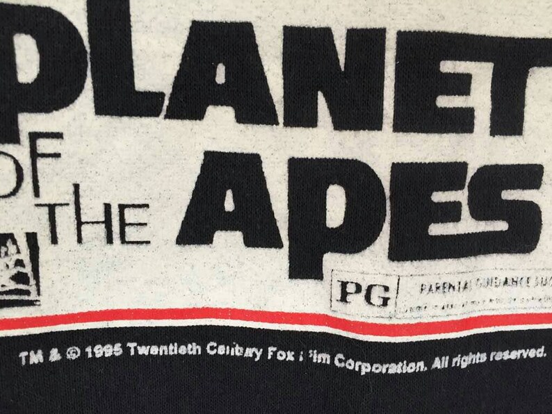 May include: Close-up of a black and white Planet of the Apes graphic. The text reads "PLANET OF THE APES" in large black letters. Below the text is a red and white stripe. The image also includes the PG rating and copyright information.