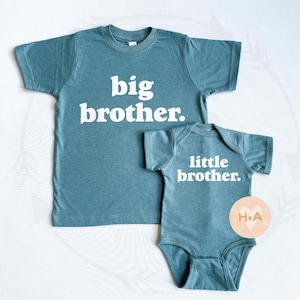 May include: Two teal blue t-shirts with white text. The larger shirt says "big brother." The smaller shirt says "little brother."
