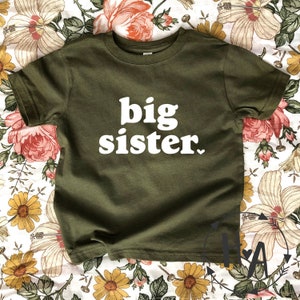 May include: A green t-shirt with the text "big sister" in white letters.