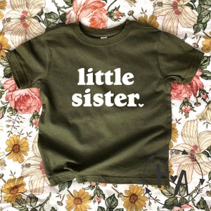 May include: A green t-shirt with the text "little sister" in white letters.