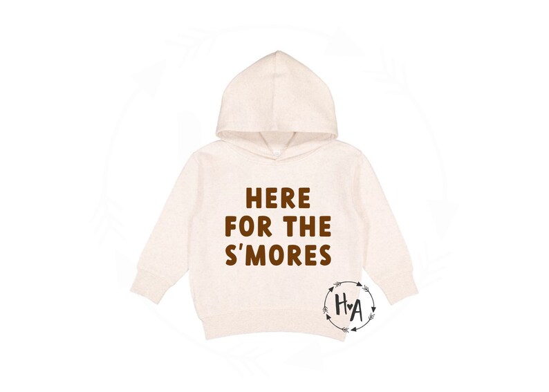 Peut inclure: Un sweat &agrave; capuche cr&egrave;me avec le texte "HERE FOR THE S'MORES" imprim&eacute; en marron sur le devant. Le sweat-shirt a un petit logo marron avec les lettres "H+A" dans un cercle avec des fl&egrave;ches de chaque c&ocirc;t&eacute;.