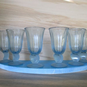 Puede incluir: Seis copas de agua vintage de color azul claro con un diseño en espiral en el tallo, dispuestas sobre una bandeja de madera semicircular azul a juego. Las copas tienen un diseño acanalado y son de cristal.