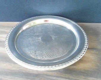 May include: A silver serving tray with a decorative embossed design. The tray has a raised rim and a scalloped edge.