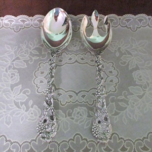 May include: A silver salad serving set with a spoon and fork. The handles are decorated with a grapevine design.